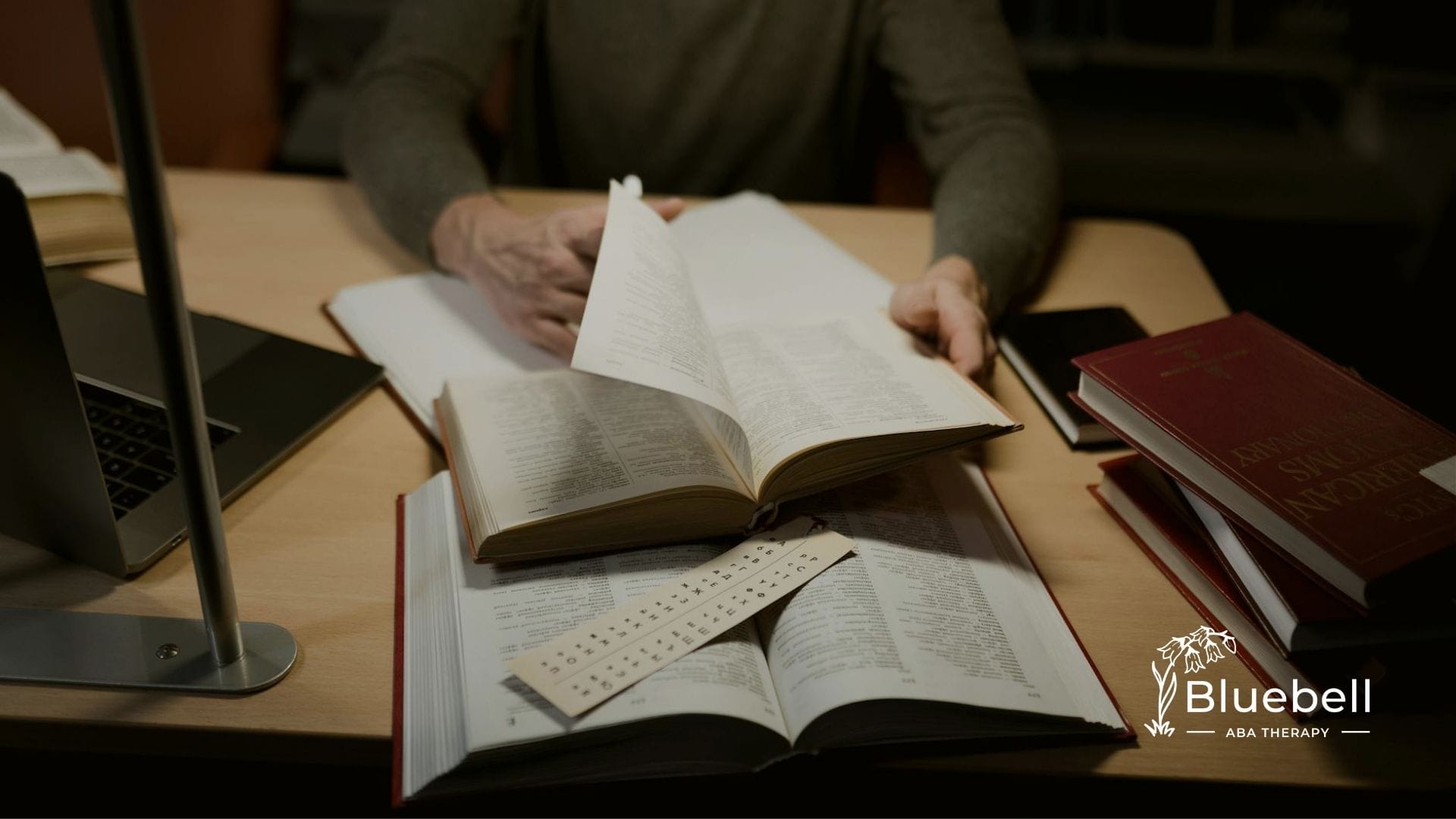 A BCBA aspirant flipping through a BCBA exam resources on a desk, surrounded by reference materials as part of their BCBA exam study guide.