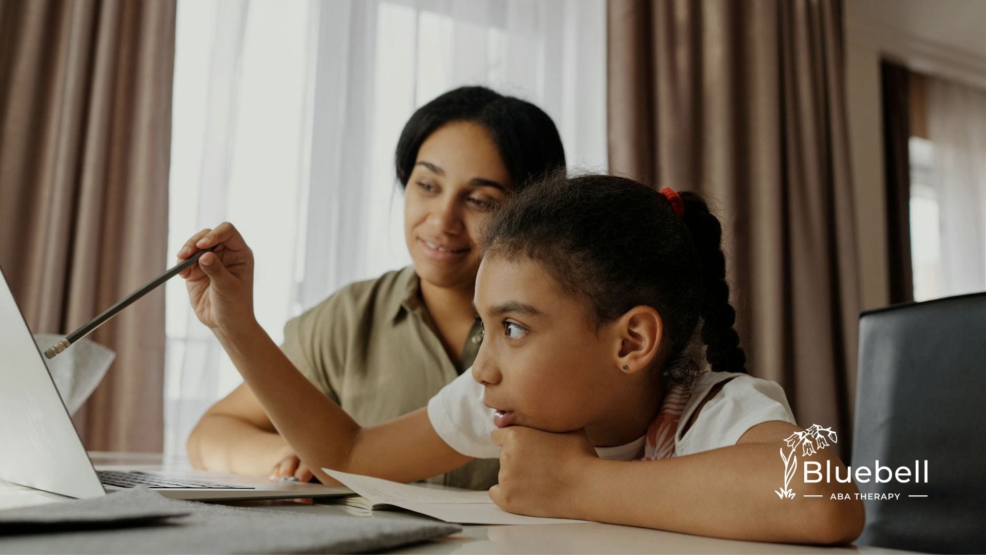 An RBT teaching a kid with autism using a laptop and notebook during home-based ABA therapy in NC.
