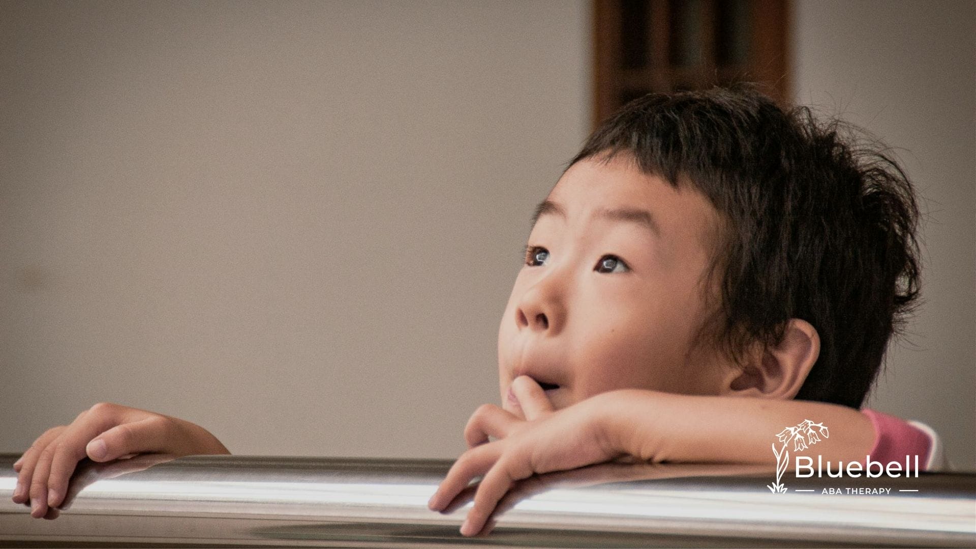 Curious autistic child leaning on a railing, looking upwards with an expression of wonder in NC.