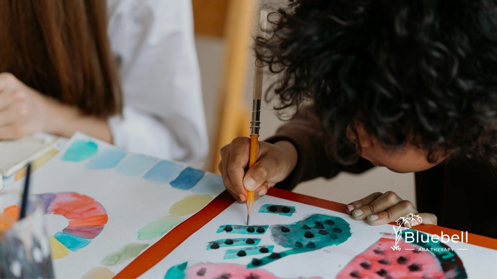 Autistic child focusing on painting vibrant patterns with watercolors on white paper at home in NC.