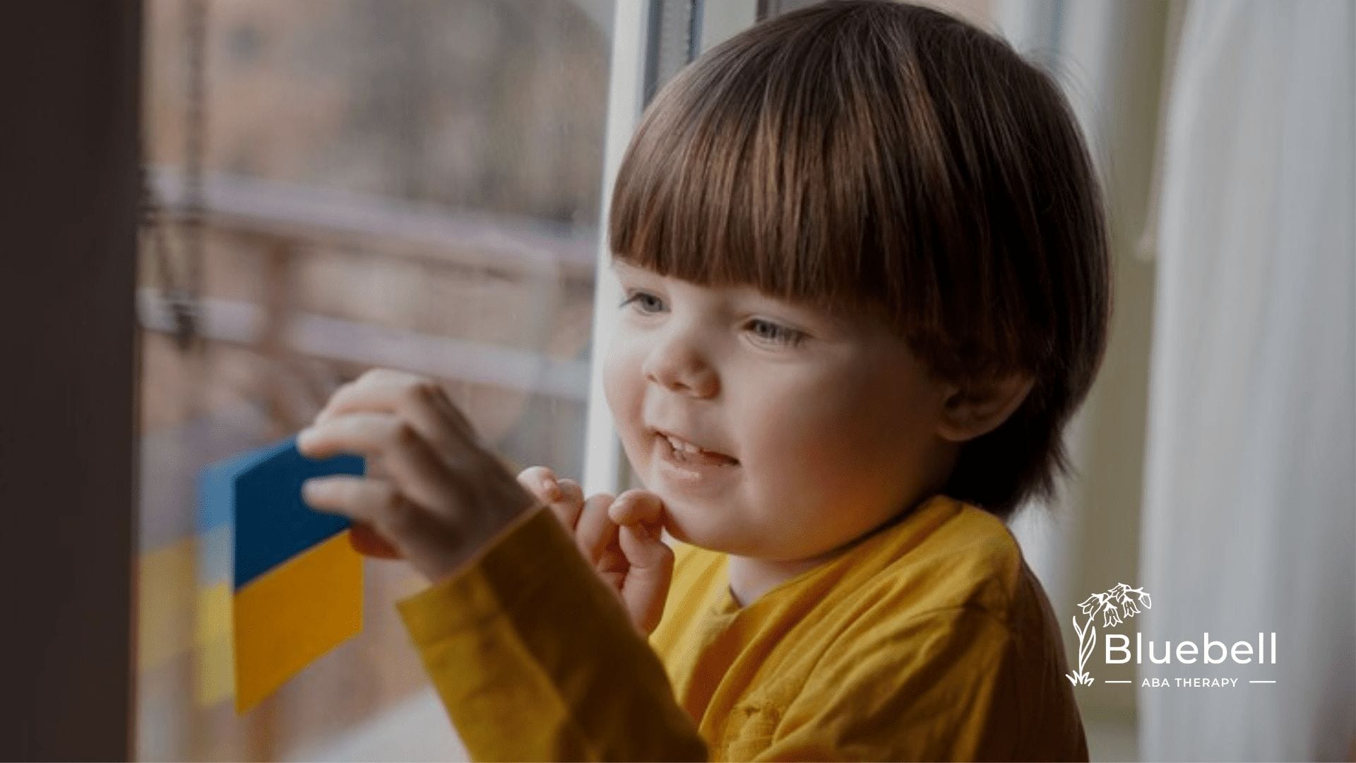 A child sticking a yellow and blue paper on a window