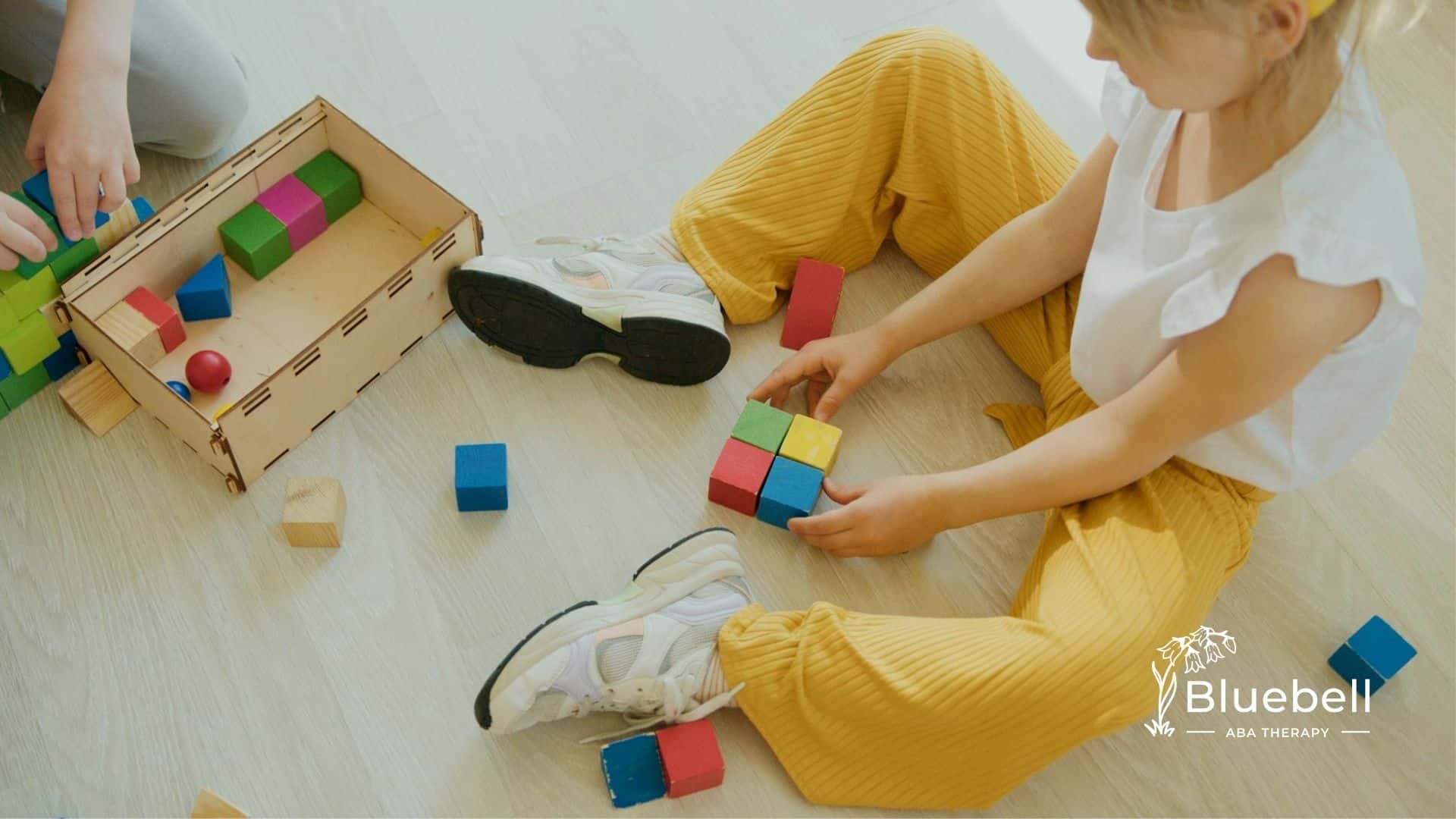 Child with autism arranging blocks on the floor, focusing on a box of toys nearby in North Carolina.