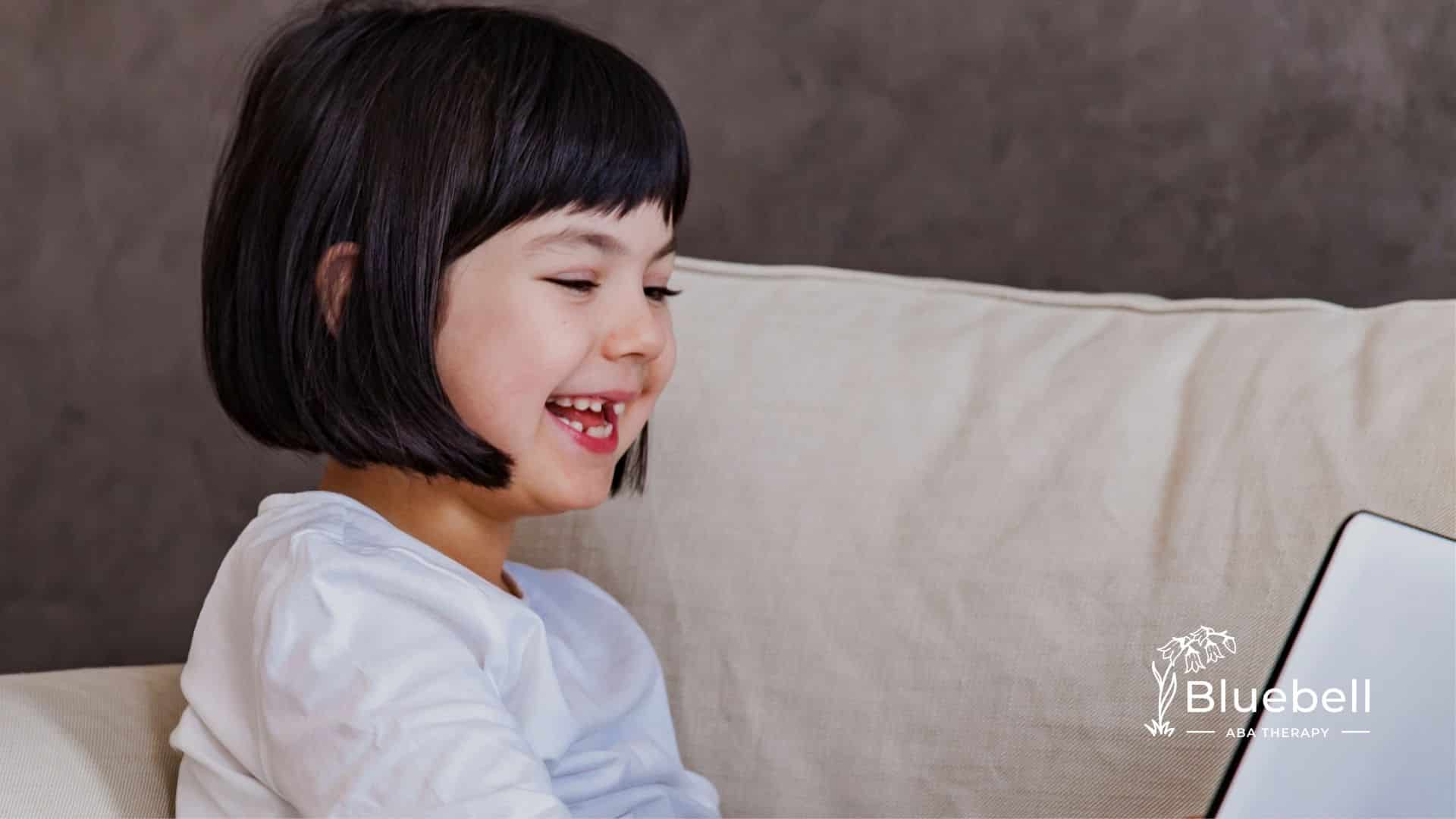 A girl with a short bob haircut laughing while looking at a laptop screen.