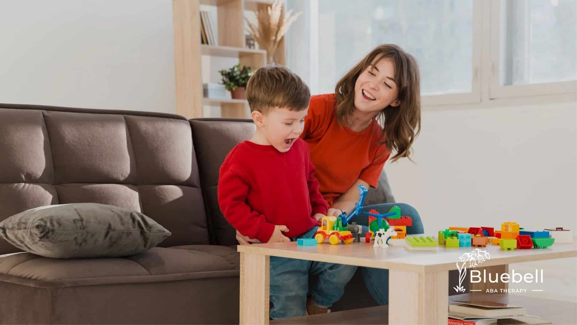 An ABA therapist and a child happily play with blocks at a table.