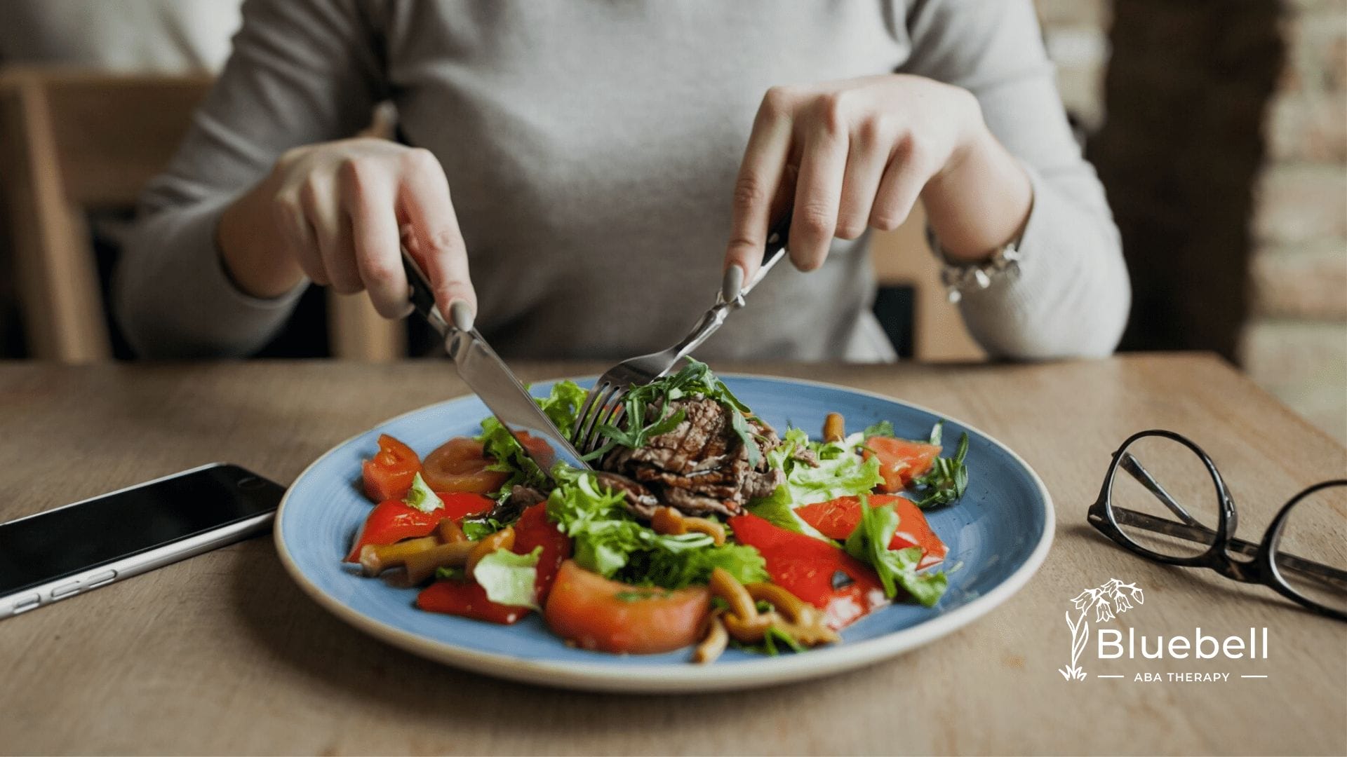 A woman eating a plate of vegetable salad using a fork and a knife