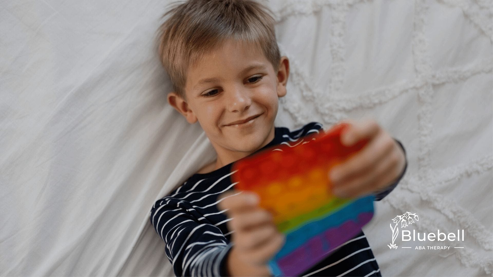 An autistic child lying on a bed holding a fidget toy