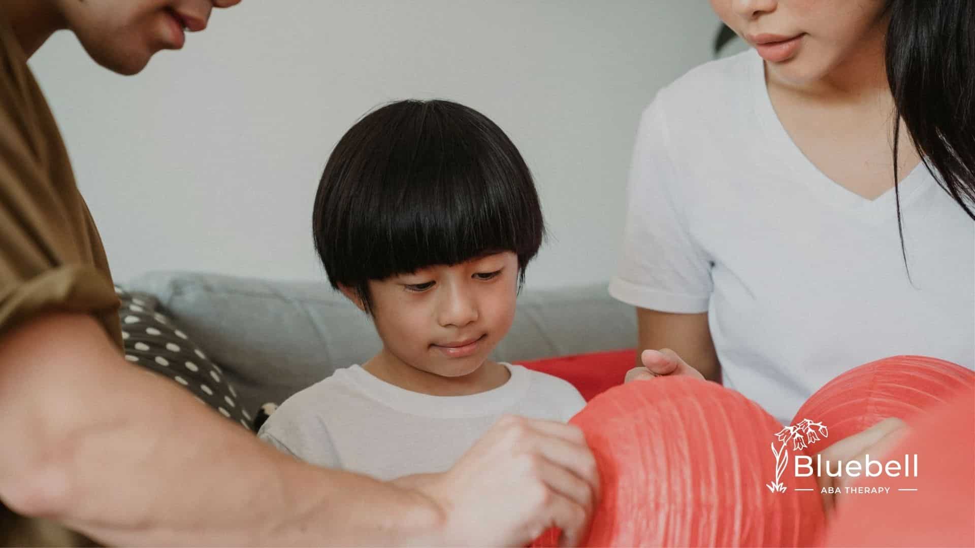 An autistic child with short black hair decorating a red paper lantern with family members in NC.