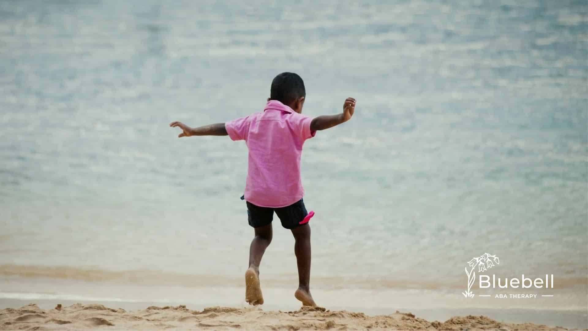 An autistic child eloping on a sandy beach near water in North Carolina wearing a pink shirt.