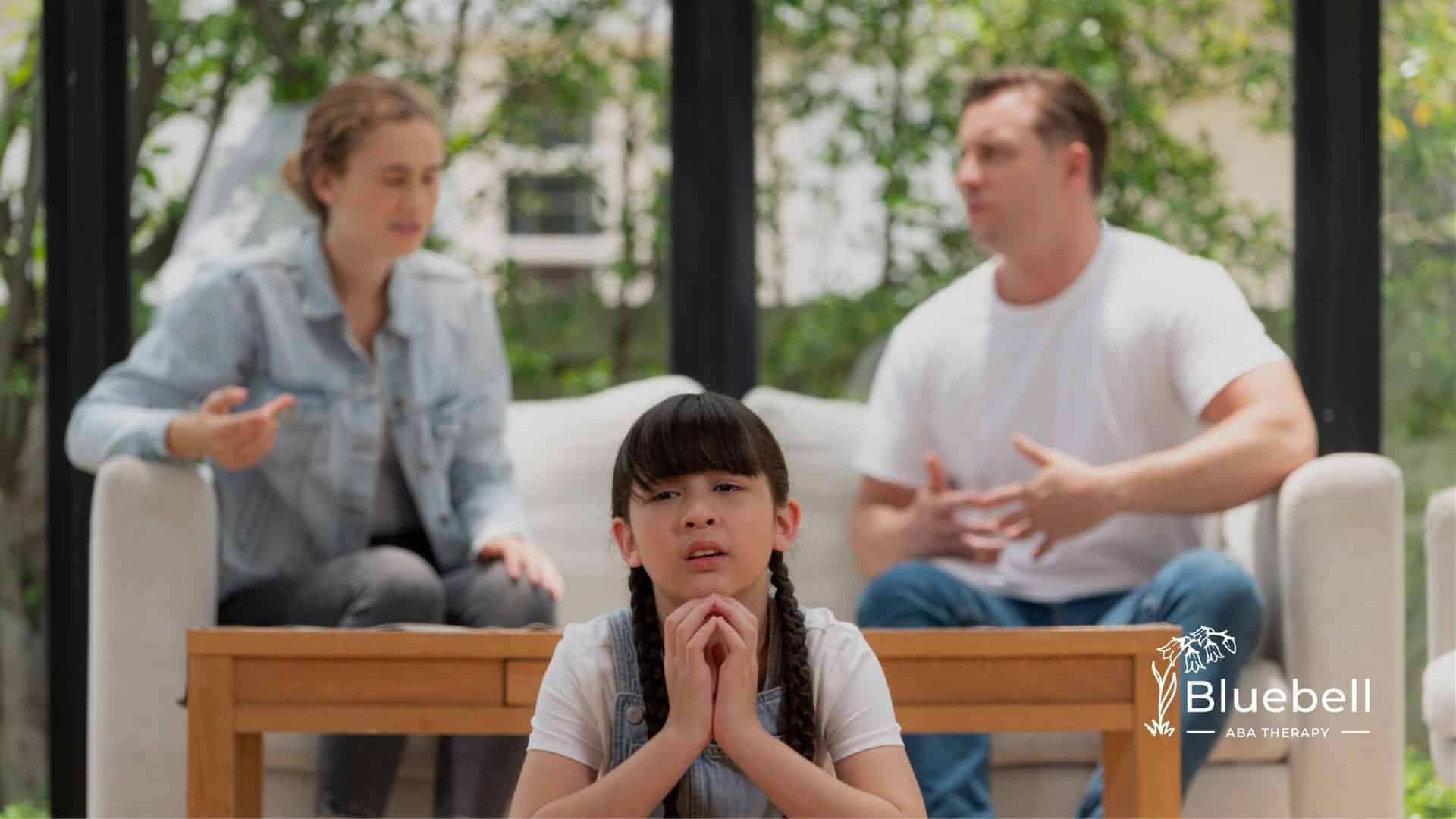 Autistic girl sitting sadly while her parents argue in the background.