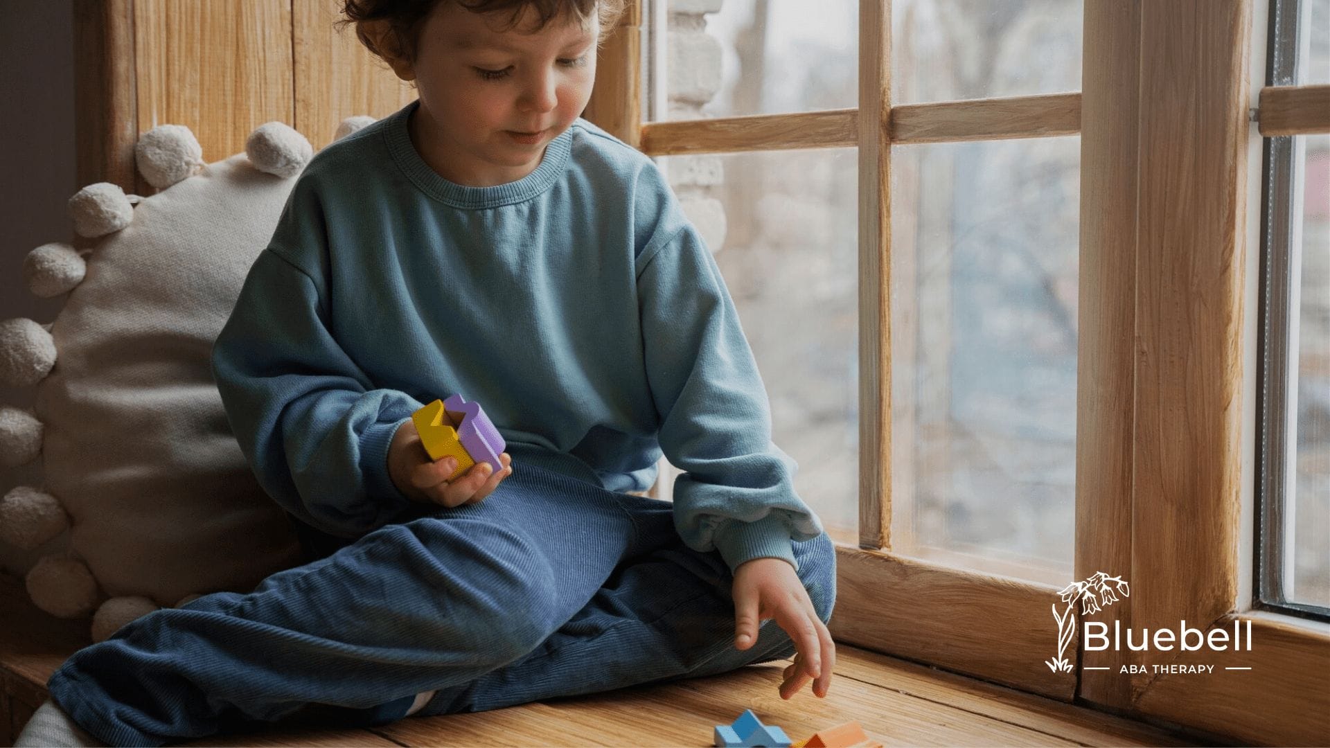 A neurodivergent child sitting in front of a window playing with colorful blocks