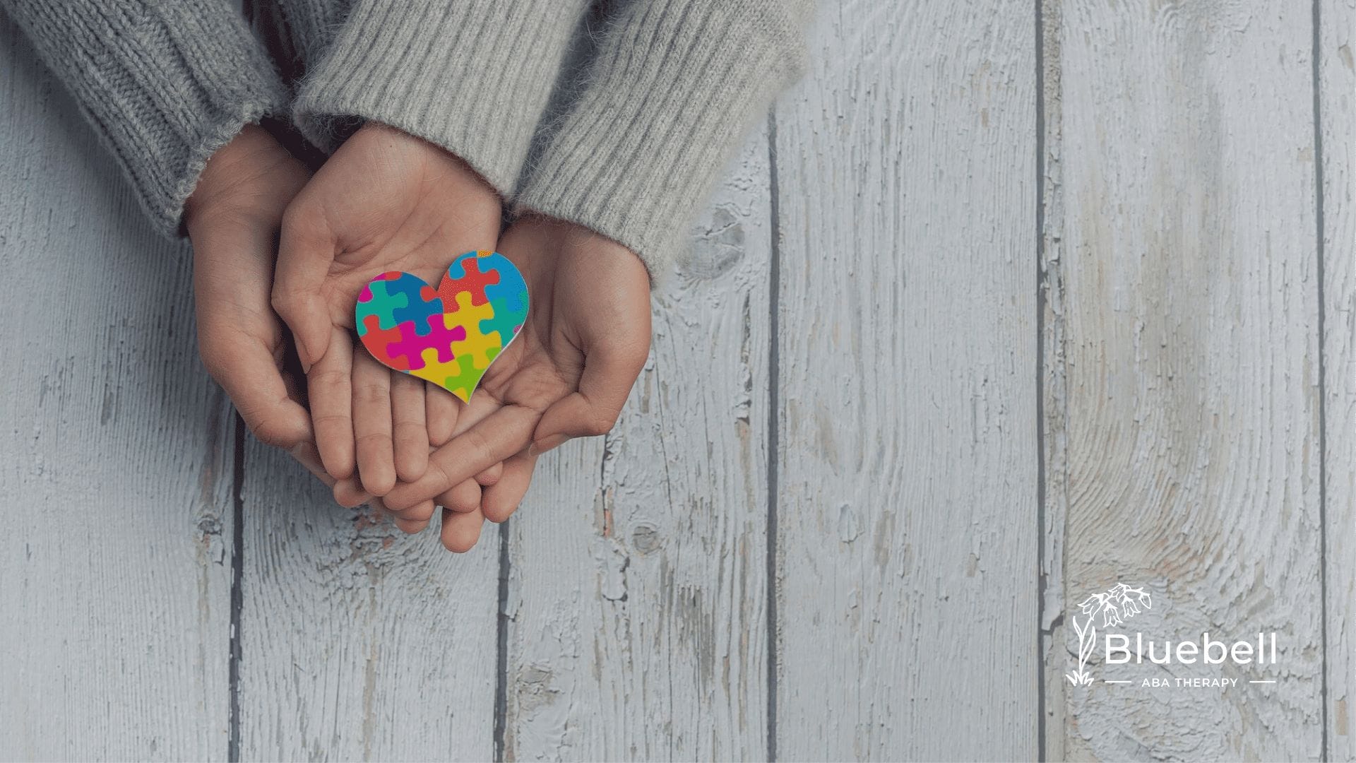 A neurodivergent kid with his parent holding hands while holding a colorful puzzle heart