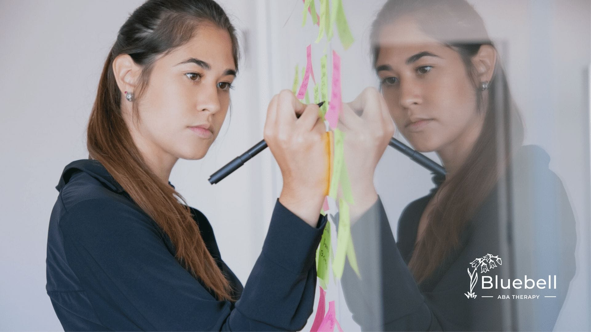 A neurodivergent woman is writing on a white board using colorful markers