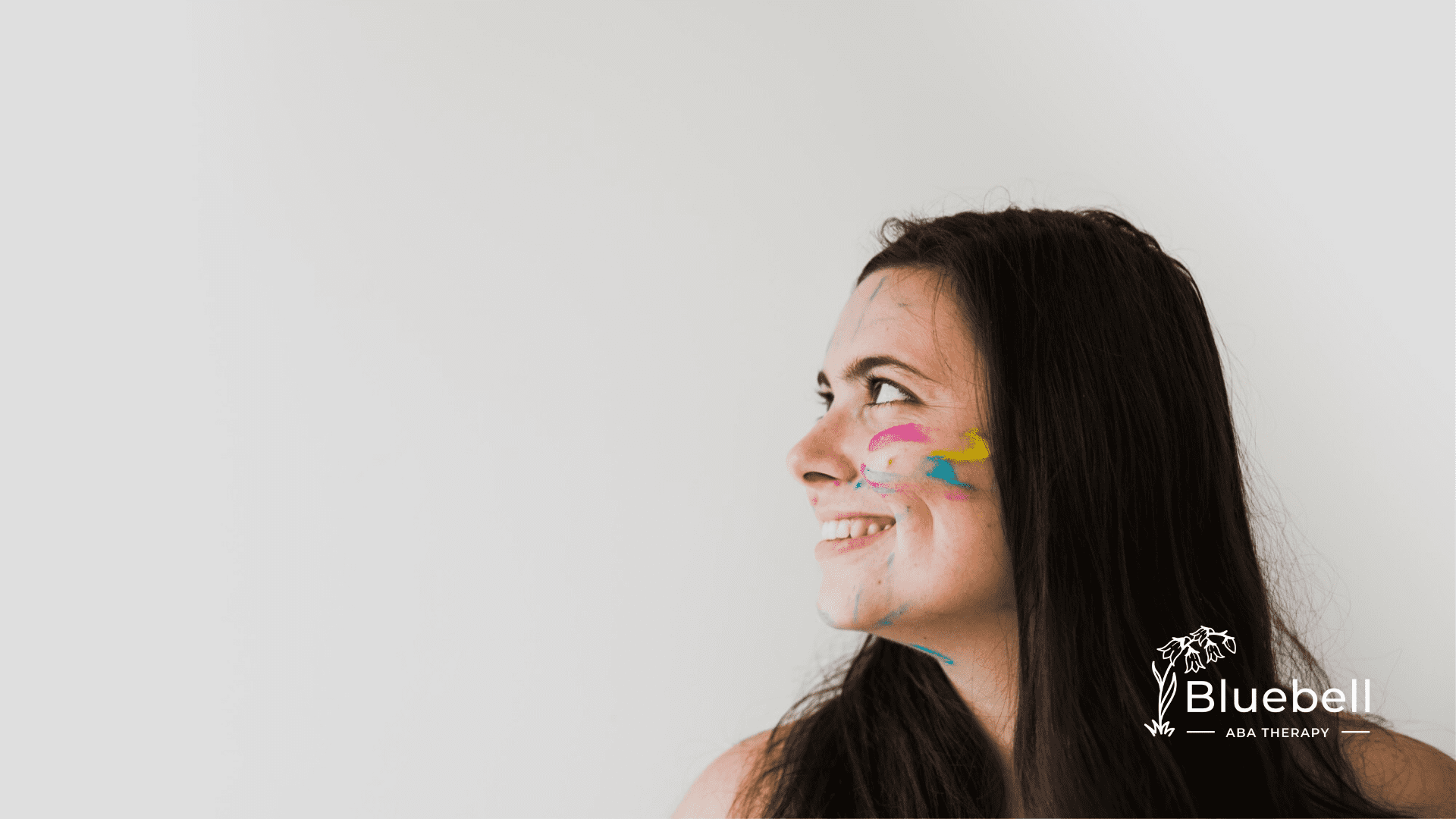A neurodivergent girl with paint on her face looking happy